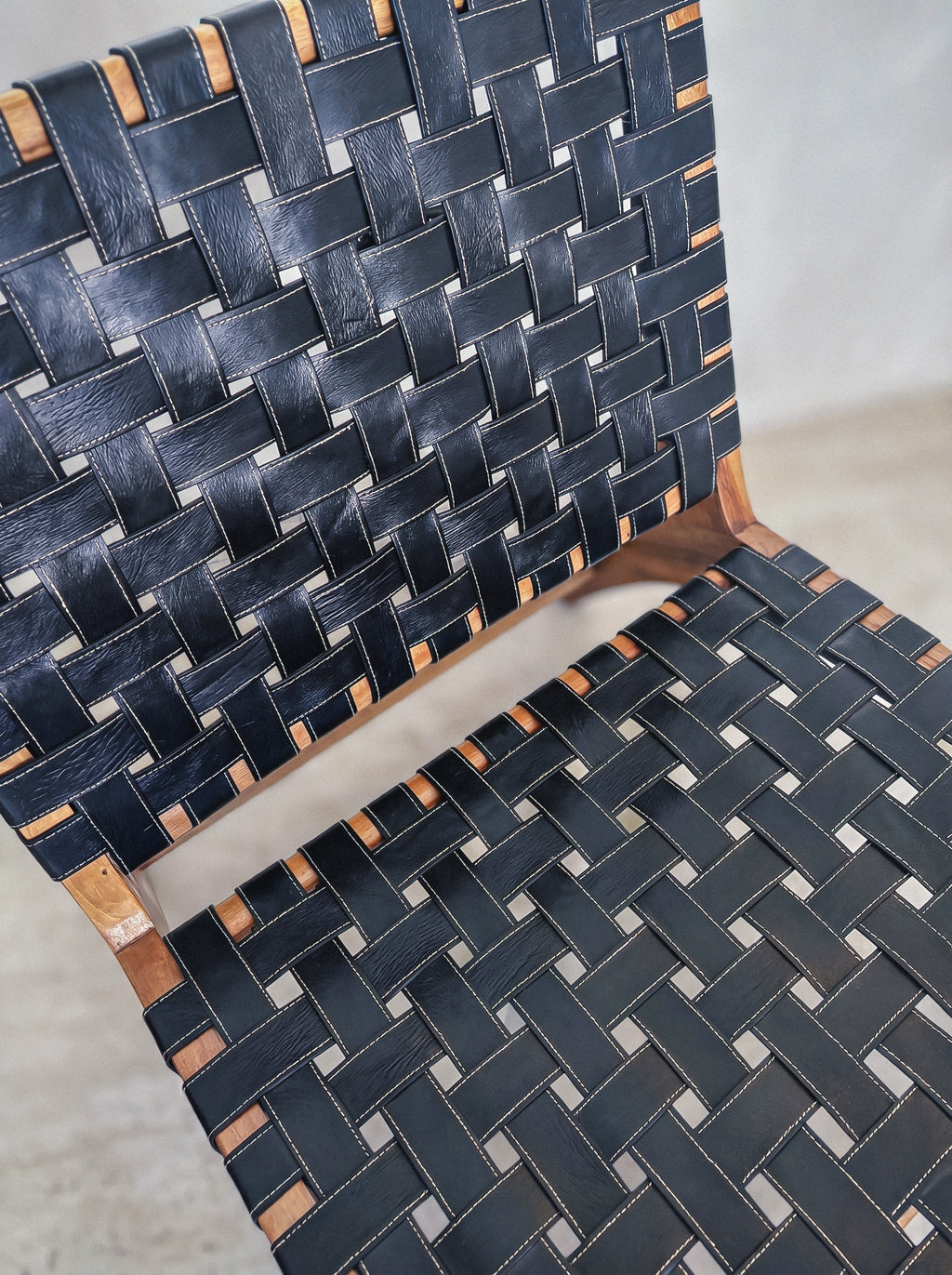 Mid-century modern lounge chair made of solid walnut wood and black woven leather straps.