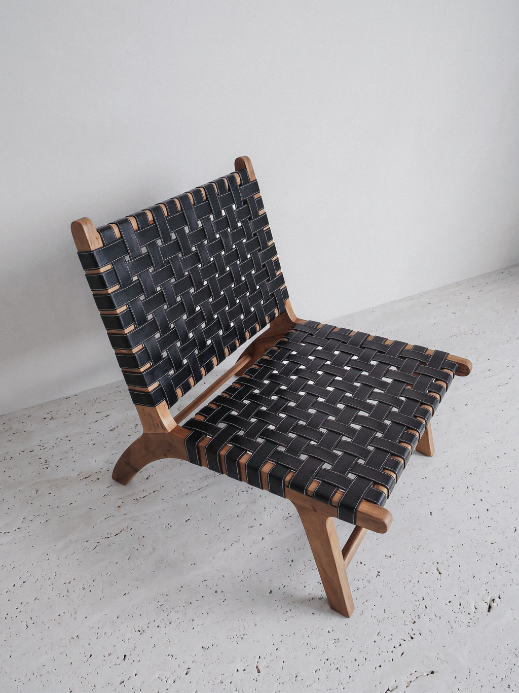 Mid-century modern lounge chair made of solid walnut wood and black woven leather straps.