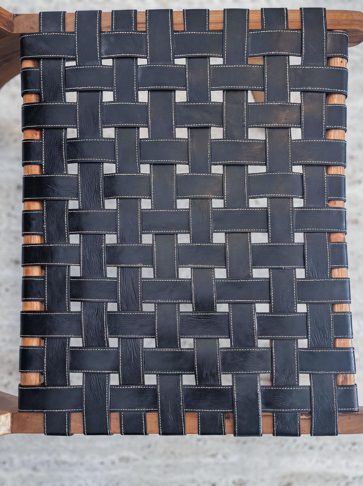 Detail of stitched black leather straps woven on the walnut lounge chair frame